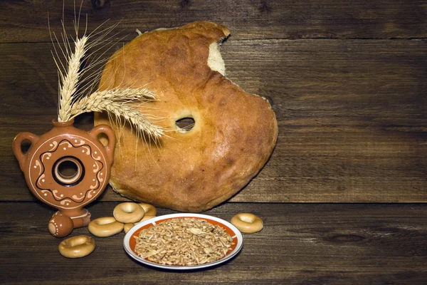 Круглая буханка хлеба, бубликов и пшеницы на фоне дерева — стоковое фото