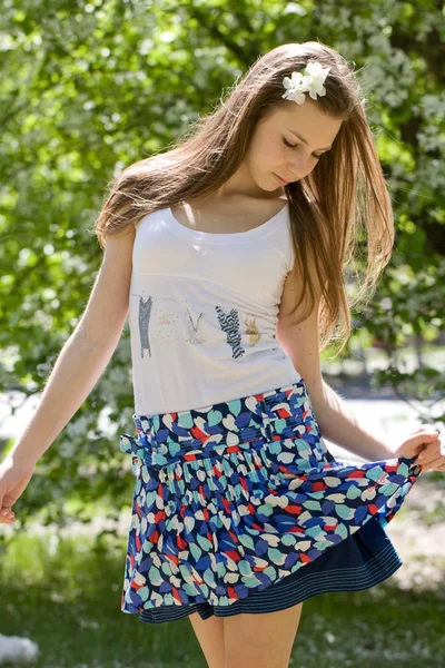 Joven hermosa chica en un jardín floreciente mira a la falda — Foto de Stock