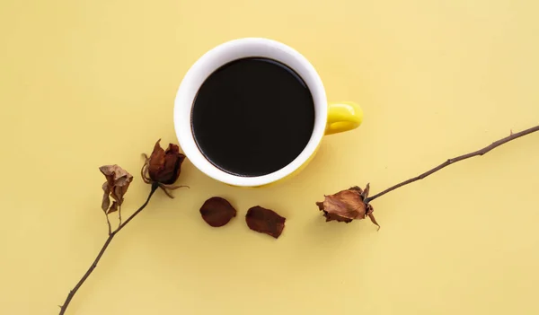 Gelbe Keramiktasse Mit Schwarzem Kaffee Zwischen Getrockneten Rosen Auf Pastellfarbenem — Stockfoto