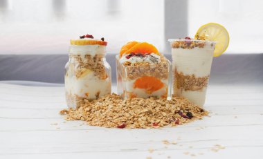 Arka planda üç bardak yoğurt karışık meyve, bol bol mısır gevreği, ev yapımı yemek, bulanık ışık.