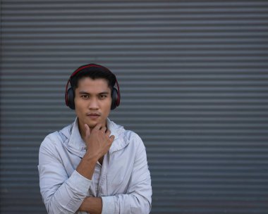 Kafasına kulaklık takan genç adam, sol elini kaldır çeneye dokun ve bak, fonun sol tarafında, bulanık ışık pozu ver.