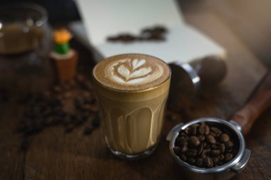 Bulanık latte sanatıyla bir bardak kahve, ahşap masa, bulanık ışık tasarımı arka plan