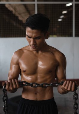 Terli vücutlu, formda ve kaslı genç bir adam elinde demir zincir, bulanık bir ışık.