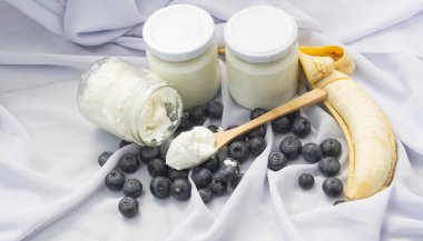 Açılmış şişe, yabanmersini ve muzun ortasına konmuş tahta kaşıkta yoğurt.