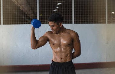 Young man with fit and firm muscle,raising dumbbell with one hand,show strong power from exercise,blurry light around