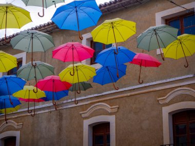 Mavi bir gökyüzünde asılı renkli şemsiyeler