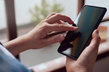 Kadın arka planda penceresi olan akıllı telefon ekranını işaret ediyor