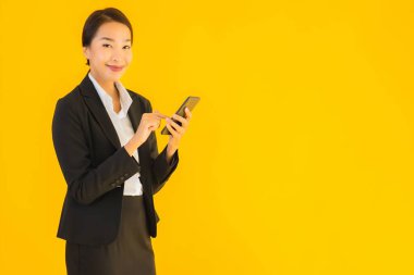 Portre güzel genç Asyalı kadın akıllı cep telefonu ve kahve fincanı ile izole edilmiş sarı arka planda