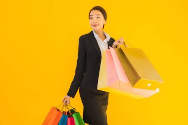 Sarı izole edilmiş arka planda alışveriş merkezinden alışveriş çantasıyla güzel bir genç Asyalı kadın portresi.
