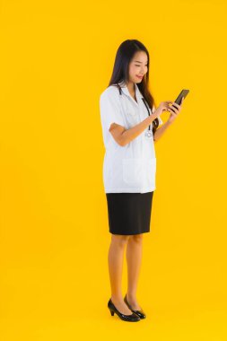 Güzel Asyalı genç doktor kadın sarı izole edilmiş arka planda akıllı cep telefonu kullanıyor.