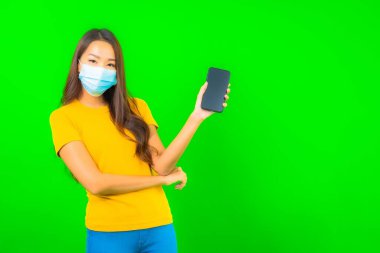 Güzel Asyalı genç bir kadının portresi, yeşil yalıtılmış arka planda kovid19 veya koronavirüsten korunmak için maske takar.
