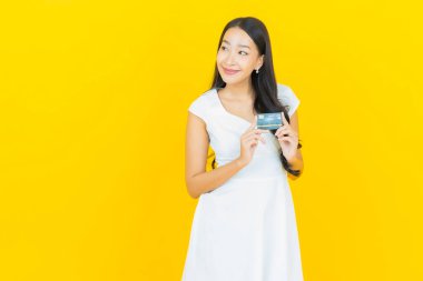 Asyalı güzel bir kadının portresi. Sarı arka planda kredi kartıyla gülümsüyor.