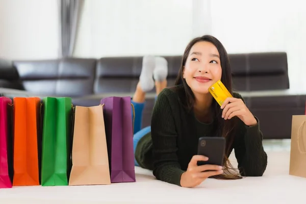 亚洲年轻貌美的女人 带着购物袋和信用卡 带着手机在家网上购物 — 图库照片