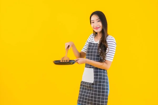 肖像画美しい若いアジアの女性は 黄色の隔離された背景に黒パンとSpatulaとエプロンを着用 — ストック写真
