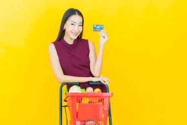 Renkli arka planda süpermarketten alınmış market sepetiyle gülümseyen güzel Asyalı kadın portresi.