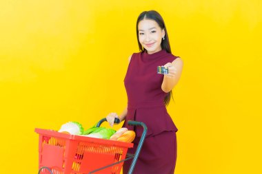 Renkli arka planda süpermarketten alınmış market sepetiyle gülümseyen güzel Asyalı kadın portresi.