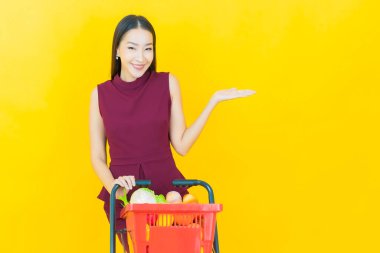 Renkli arka planda süpermarketten alınmış market sepetiyle gülümseyen güzel Asyalı kadın portresi.