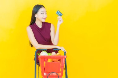 Renkli arka planda süpermarketten alınmış market sepetiyle gülümseyen güzel Asyalı kadın portresi.