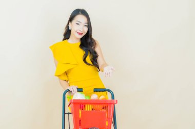 Renkli arka planda süpermarketten alınmış market sepetiyle gülümseyen güzel Asyalı kadın portresi.