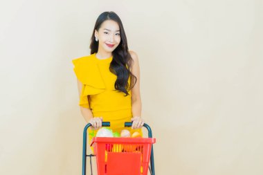 Renkli arka planda süpermarketten alınmış market sepetiyle gülümseyen güzel Asyalı kadın portresi.