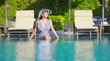 Güzel bir Asyalı kadın portresi tatil köyünde yüzme havuzunda rahatlıyor.