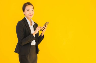 Portre güzel genç Asyalı kadın akıllı cep telefonu ve kahve fincanı ile izole edilmiş sarı arka planda