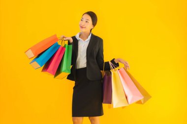 Sarı izole edilmiş arka planda alışveriş merkezinden alışveriş çantasıyla güzel bir genç Asyalı kadın portresi.
