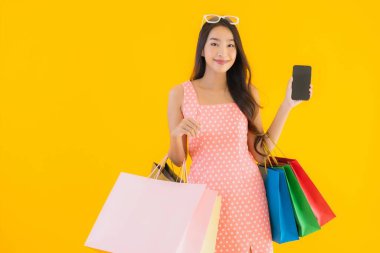 Renkli alışveriş çantalı güzel Asyalı kadın akıllı cep telefonu ve sarı izole edilmiş arka planda kredi kartı.