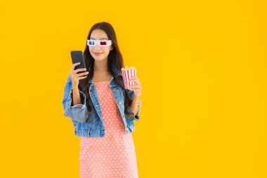 Güzel bir Asyalı kadın portresi telefon patlamış mısırı ve sarı izole edilmiş bir arka planda film izlemekten memnun.
