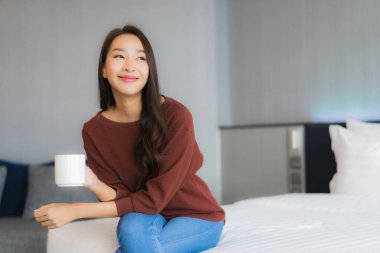 Yatak odasında, yatağında kahve fincanı olan güzel Asyalı kadın portresi.