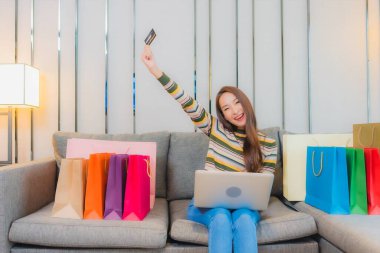 Asyalı güzel bir kadının portresi kanepeye dizüstü bilgisayar kullanıyor.