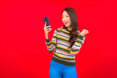 Kırmızı arka planda akıllı cep telefonlu güzel Asyalı kadın portresi.