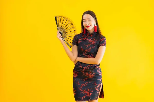 肖像美しい若いアジアの女性は黄色の孤立した背景に中国の新年のコンセプトのためのファンと中国のドレスを身に着けている — ストック写真