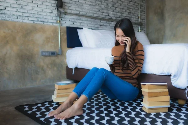 Young asian woman using smart mobile phone with read book and coffee cup in bedroom interior