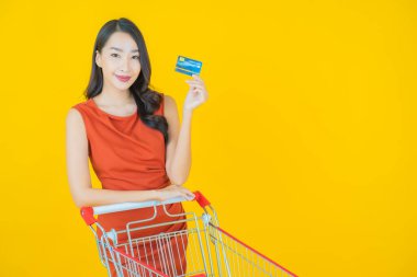 Renkli arka planda süpermarketten alınmış market sepetiyle gülümseyen güzel Asyalı kadın portresi.