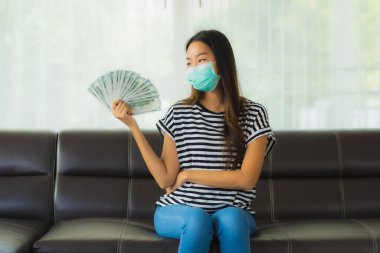 Maskeli güzel Asyalı kadının portresi evde para ya da para gösteriyor.