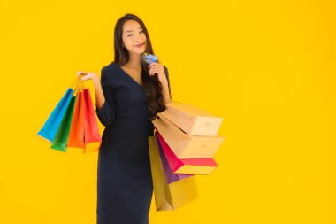 Portre güzel genç Asyalı kadın alışveriş çantası kredi kartı ve akıllı cep telefonu sarısı izole bir arka plan.