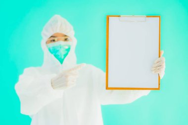 Güzel, genç Asyalı doktor kadın koronavirüsten korunmak için ppe ya da kişisel koruyucu ekipman takıyor ya da mavi izole arka planda beyaz kartı olan 19. bölgede yaşıyor.