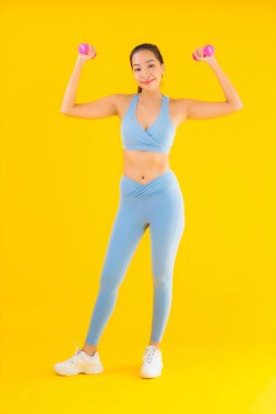 Dambıl ve spor giysili güzel Asyalı kadın sarı izole arka planda egzersize hazır.