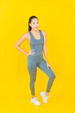Sarı arka planda spor kıyafetleri olan güzel Asyalı kadın portresi egzersize hazır.