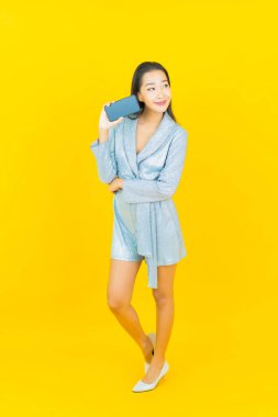 Asyalı güzel bir kadının portresi sarı arka planda akıllı cep telefonuyla gülümsüyor.