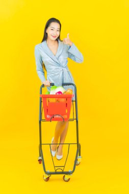 Asyalı güzel bir kadının portresi. Sarı arka planda süpermarketten alınmış alışveriş sepetiyle gülümsüyor.