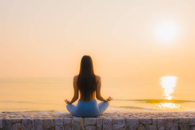 Genç Asyalı kadının portresi sağlık için gün doğumunda deniz kıyısı okyanusunda meditasyon yapıyor.