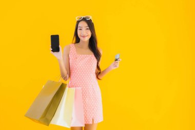 Renkli alışveriş çantalı güzel Asyalı kadın akıllı cep telefonu ve sarı izole edilmiş arka planda kredi kartı.