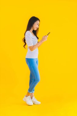 Güzel bir Asyalı kadın portresi sarı izole edilmiş arka planda akıllı cep telefonu kullanıyor.