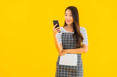 Güzel bir Asyalı kadın portresi sarı izole edilmiş arka planda akıllı cep telefonu kullanıyor.