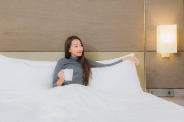 Yatak odasında, yatağında kahve fincanı olan güzel Asyalı kadın portresi.