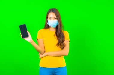 Güzel Asyalı genç bir kadının portresi, yeşil yalıtılmış arka planda kovid19 veya koronavirüsten korunmak için maske takar.