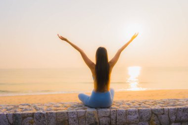 Genç Asyalı kadının portresi sağlık için gün doğumunda deniz kıyısı okyanusunda meditasyon yapıyor.