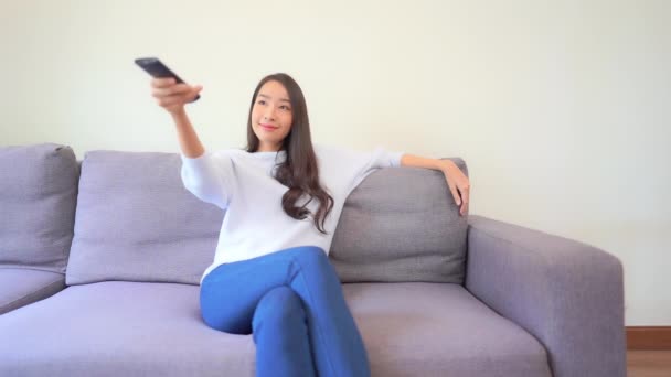 自宅で遠隔操作でテレビを見ている美しいアジアの女性の映像 — ストック動画